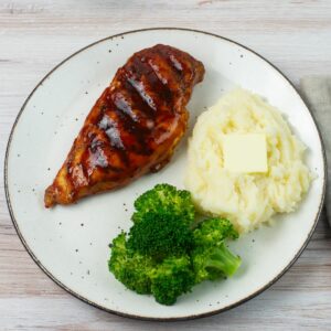 Honey Buffalo BBQ sauce used to glaze a grilled chicken breast served on a plate with potatoes and broccoli.