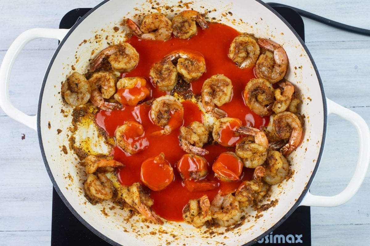 Large seasoned shrimp in a hot skillet with Buffalo sauce poured over them. 