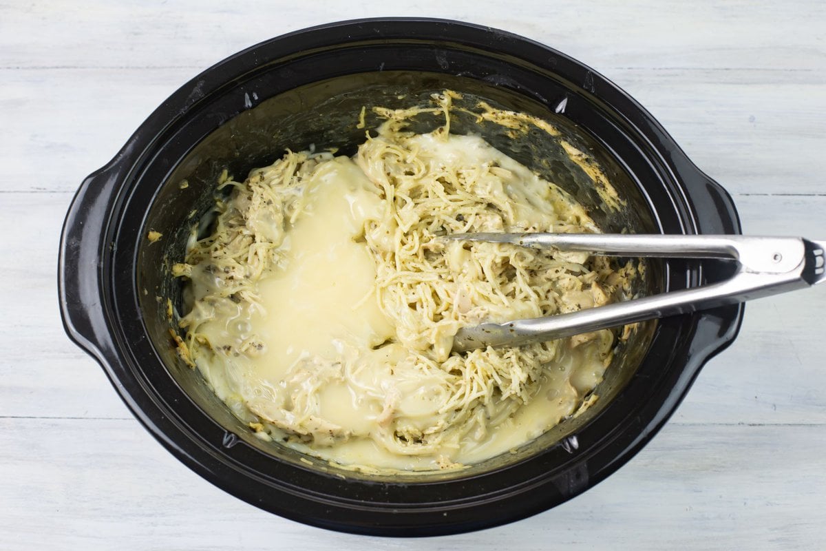 Overhead image looking down into a slow cooker filled with Pesto Chicken with melted cheese on top.