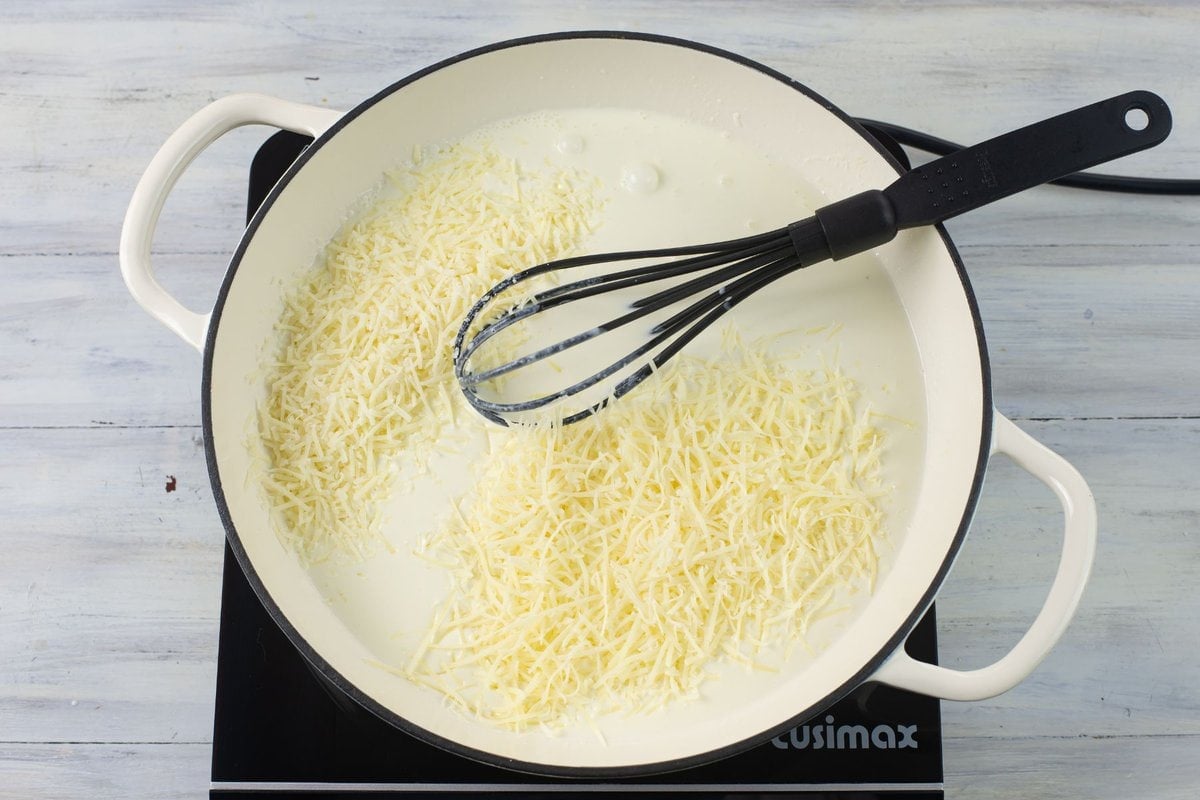 Adding shredded Parmesan and Romano cheese to the white sauce base in a skillet.