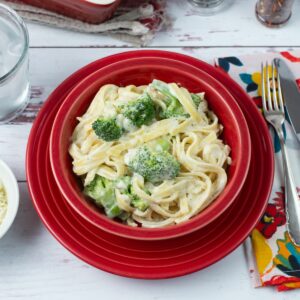 Broccoli Fettuccine Alfredo served in a red bowl with bread and salad.