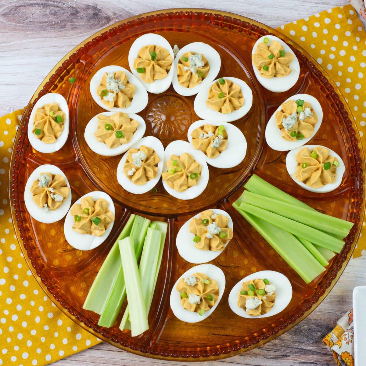 Buffalo Deviled Eggs garnished with blue cheese and sliced green onion served on a deviled egg plate.