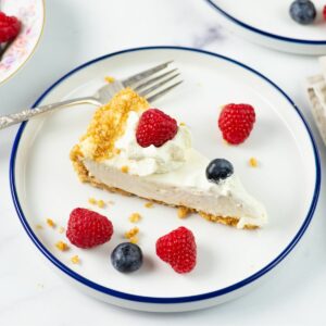 A slice of Cheesecake made with a filling with condensed milk garnished with cracker crumbs, fresh berries and whipped cream.