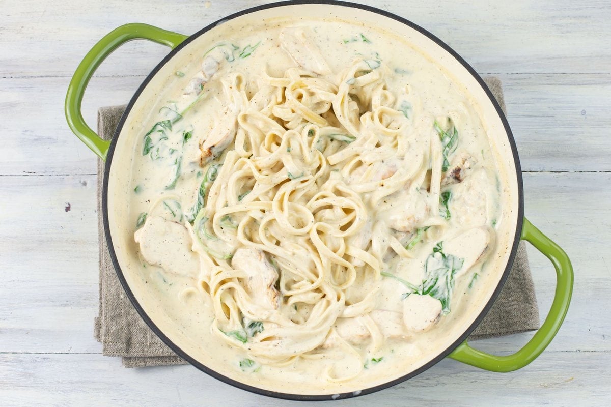 Chicken spinach alfredo sauce tossed with fettuccine noodle in a skillet.