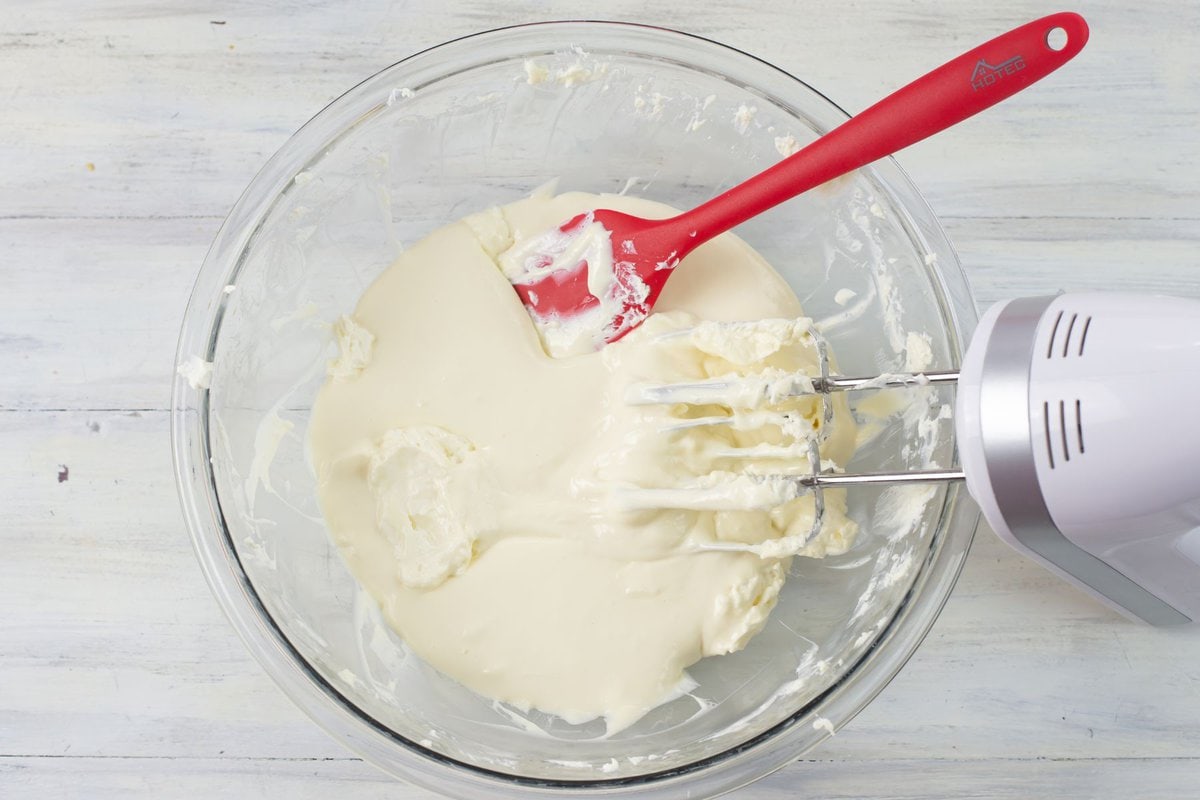 Adding the sweetended condensed milk to the bowl of beaten cream cheese.