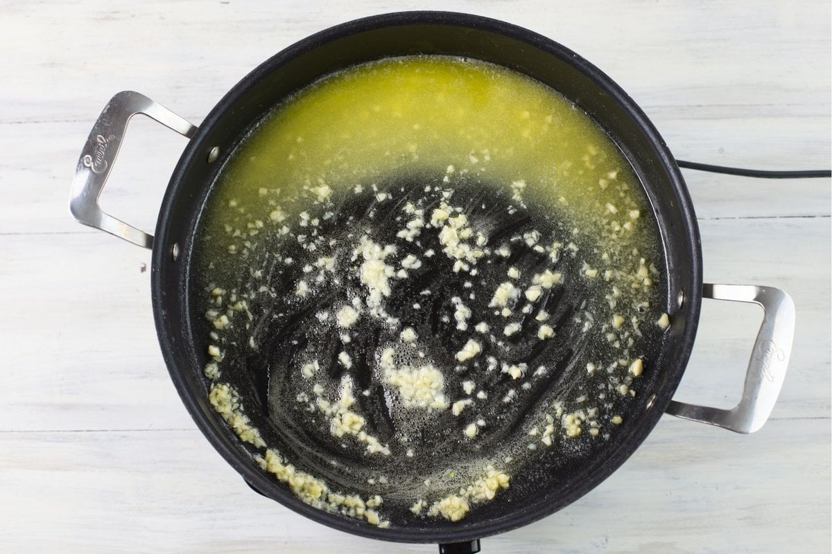 Cooking minced garlic in melted butter in a large skillet.