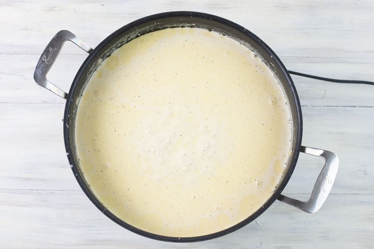 Creamy alfredo sauce boiling gently in a skillet.