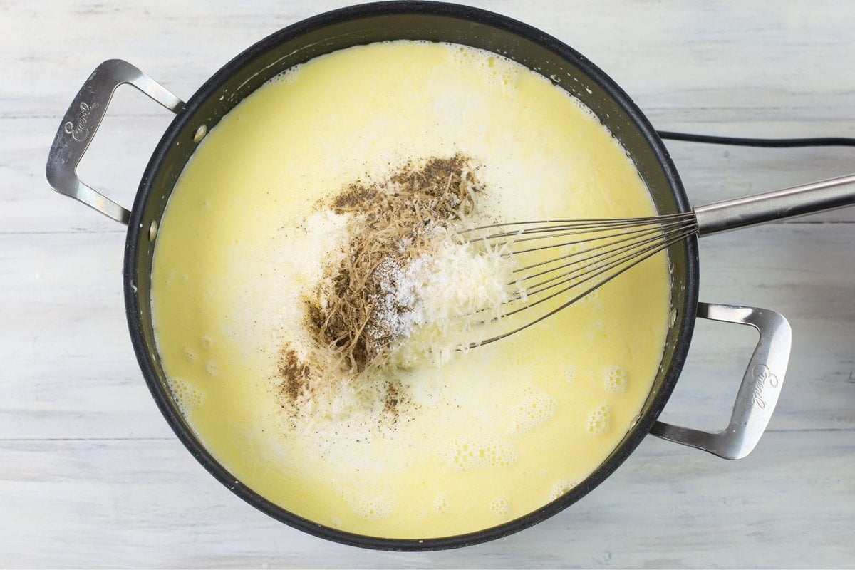 Combining shredded Parmesan cheese with Alfredo sauce ingredients in a large skillet.