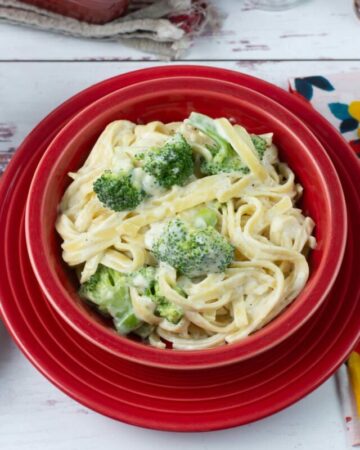 Broccoli Fettuccine Alfredo served in a red bowl with bread and salad.