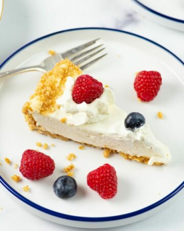 A slice of Cheesecake made with a filling with condensed milk garnished with cracker crumbs, fresh berries and whipped cream.
