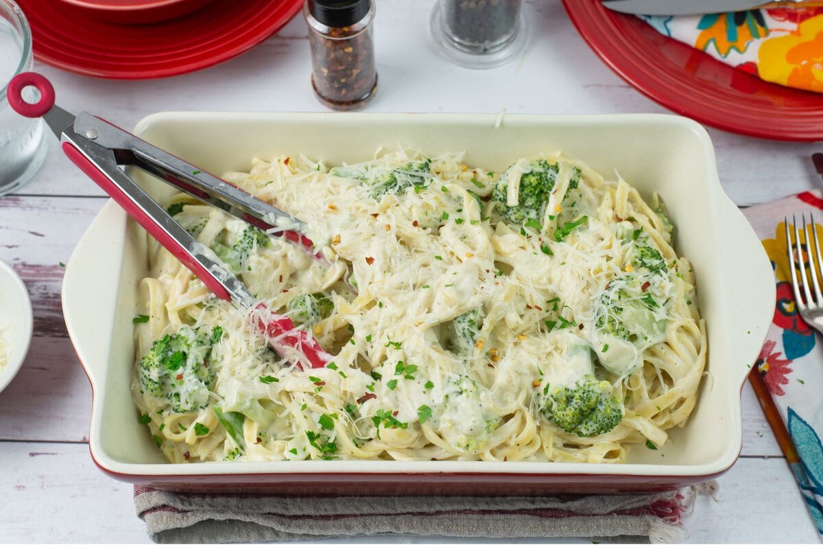 Broccoli Alfredo Pasta garnished with shredded cheese and parsley served in a casserole dish.