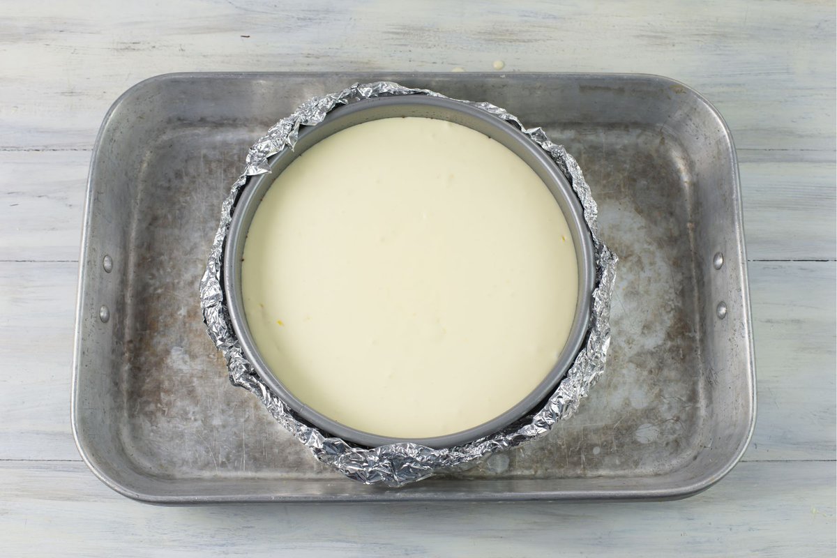Cheesecake pan filled with lemon cheesecake filling placed down into the center of a roasting pan before baking.