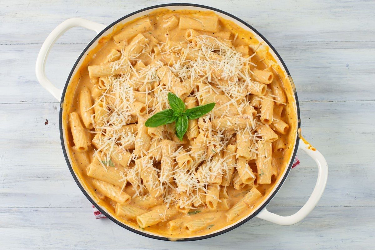 A large skillet filled with Parma Rosa Pink sauce pasta garnished with shredded cheese and fresh basil.