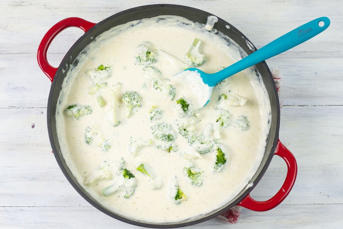 Mixing broccoli florets with homemade alfredo sauce.