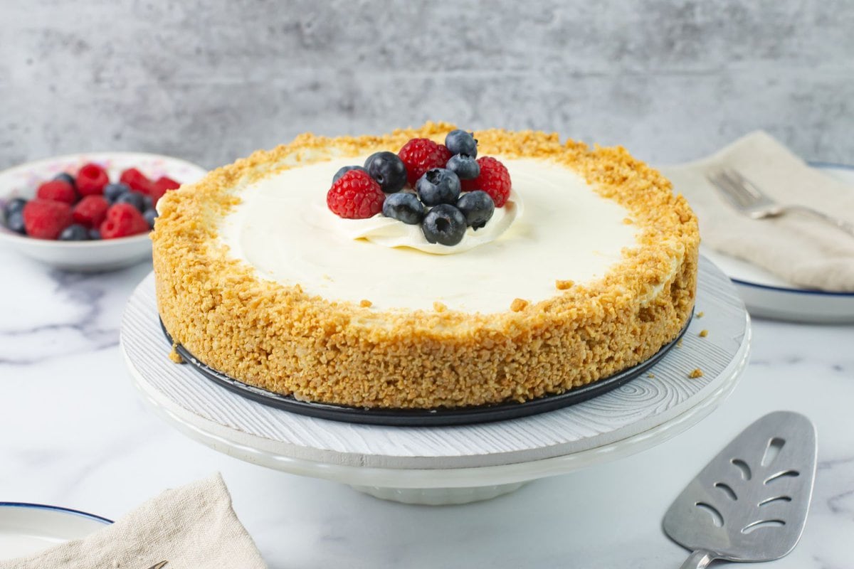 Uncut cheesecake on a cake stand with berries piled in the center.