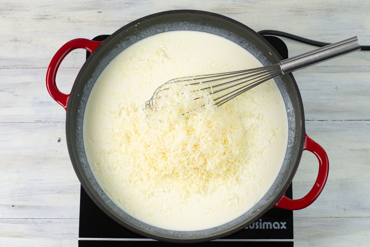 Adding shredded Parmesan cheese to the white sauce in a skillet.