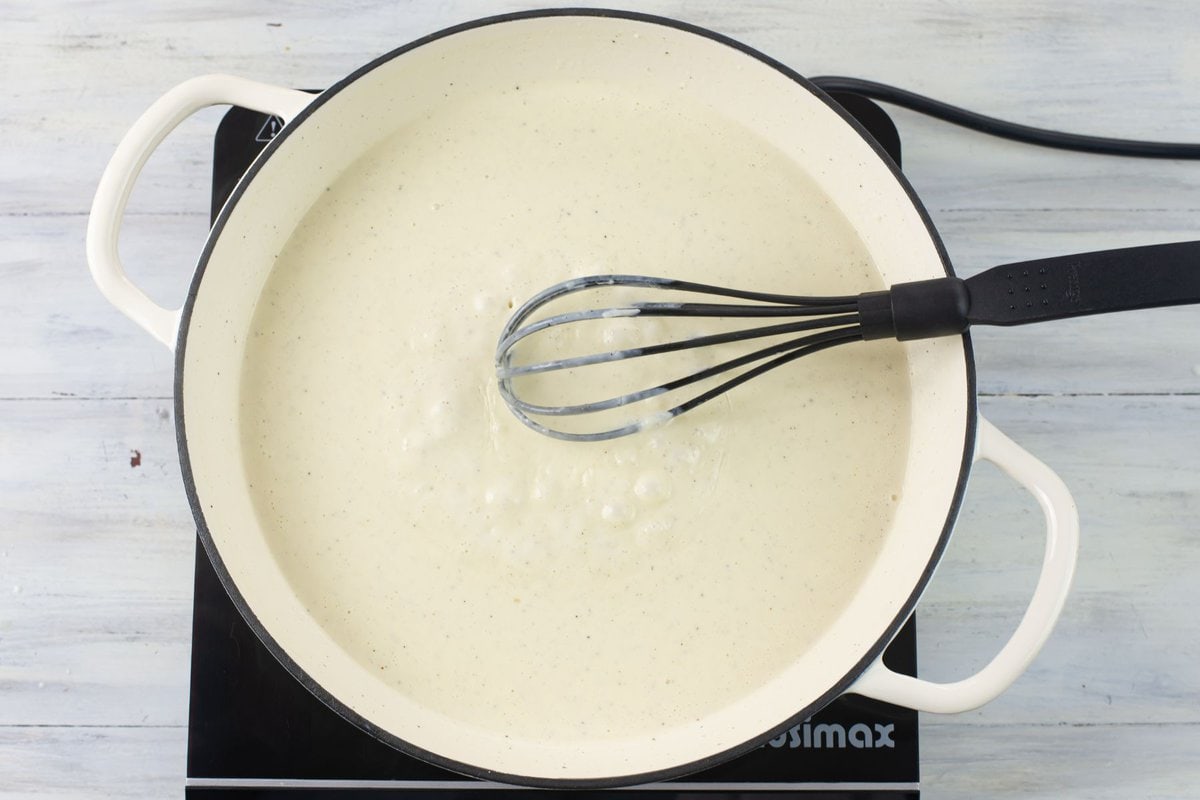 Gently bubbling alfredo sauce in a skillet.