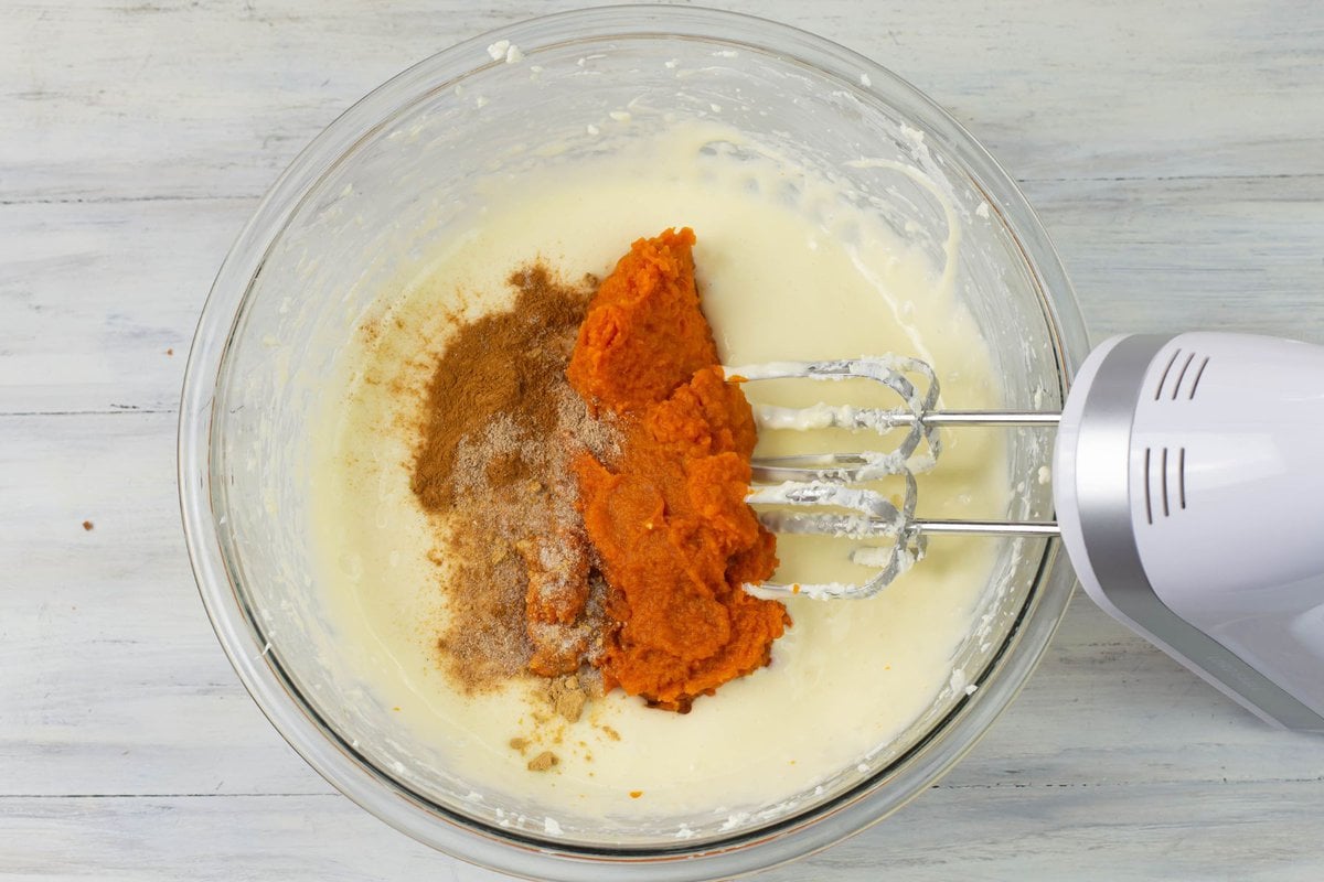Adding the pumpkin and spices to the bowl of cheesecake ingredients.