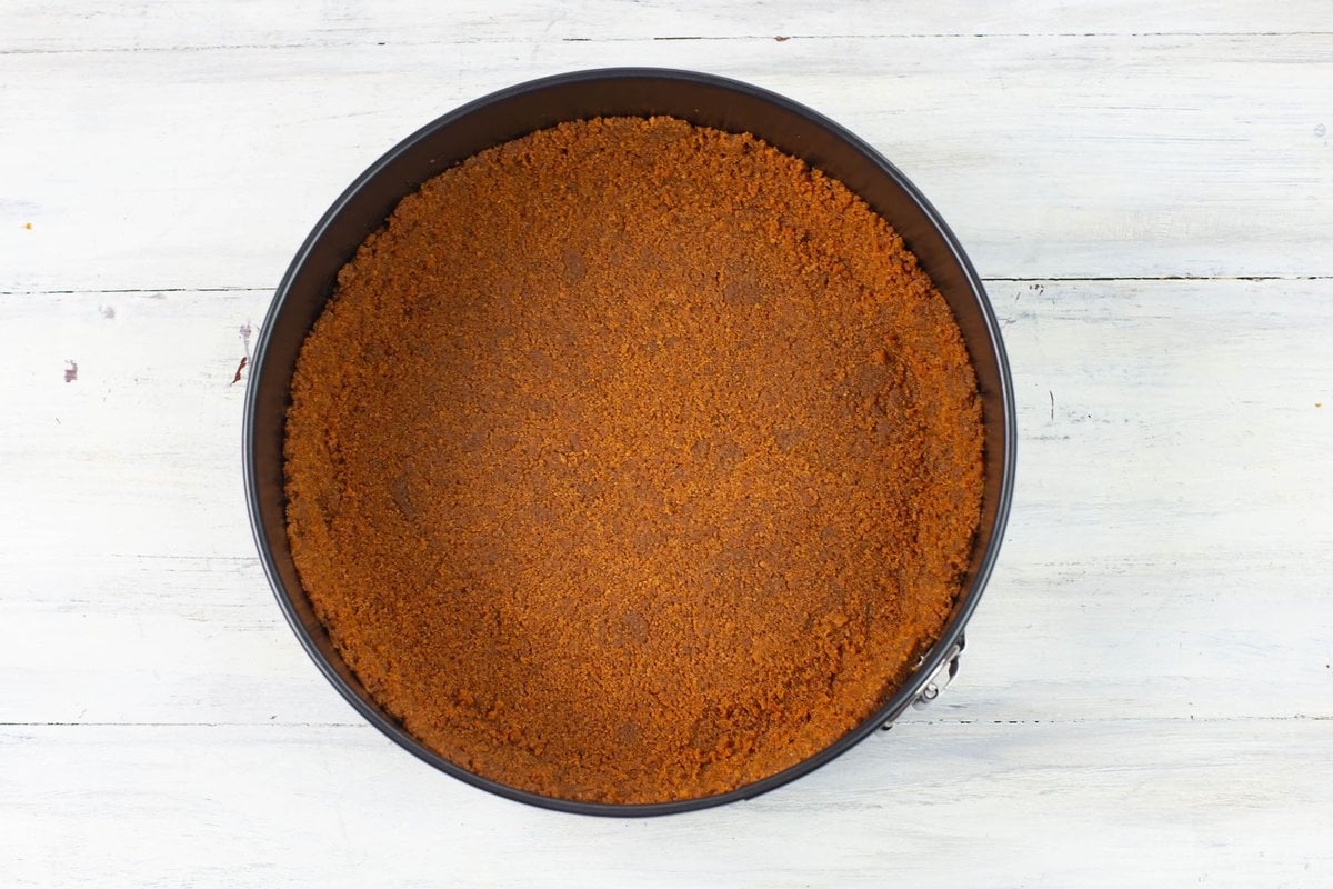 A cheesecake crust made of Biscoff cookies in a springform pan.