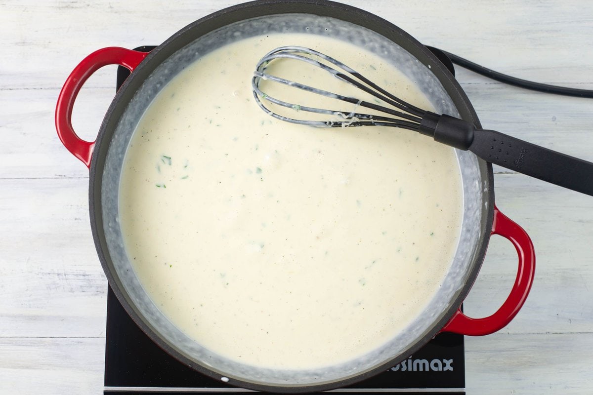 The thickened alfredo sauce in a skillet.
