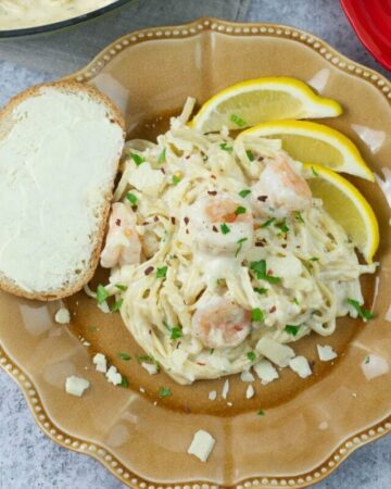 Shrimp Scampi Alfredo pasta dish served on a dinner plate with a slice of Italian bread.