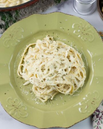 A creamy roasted garlic alfredo served over pasta on a green dinner plate.