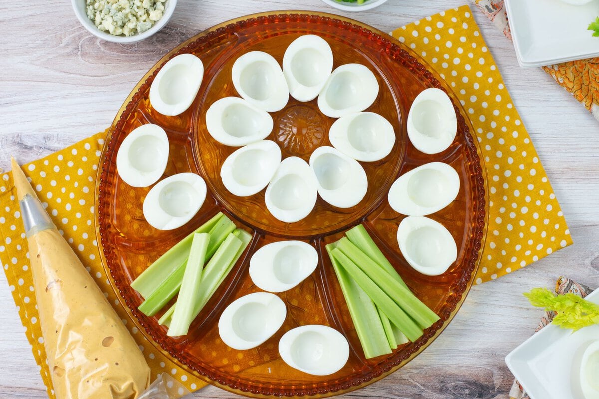 A glass deviled egg plate with eggs cut in half before filling with buffalo deviled egg filling.