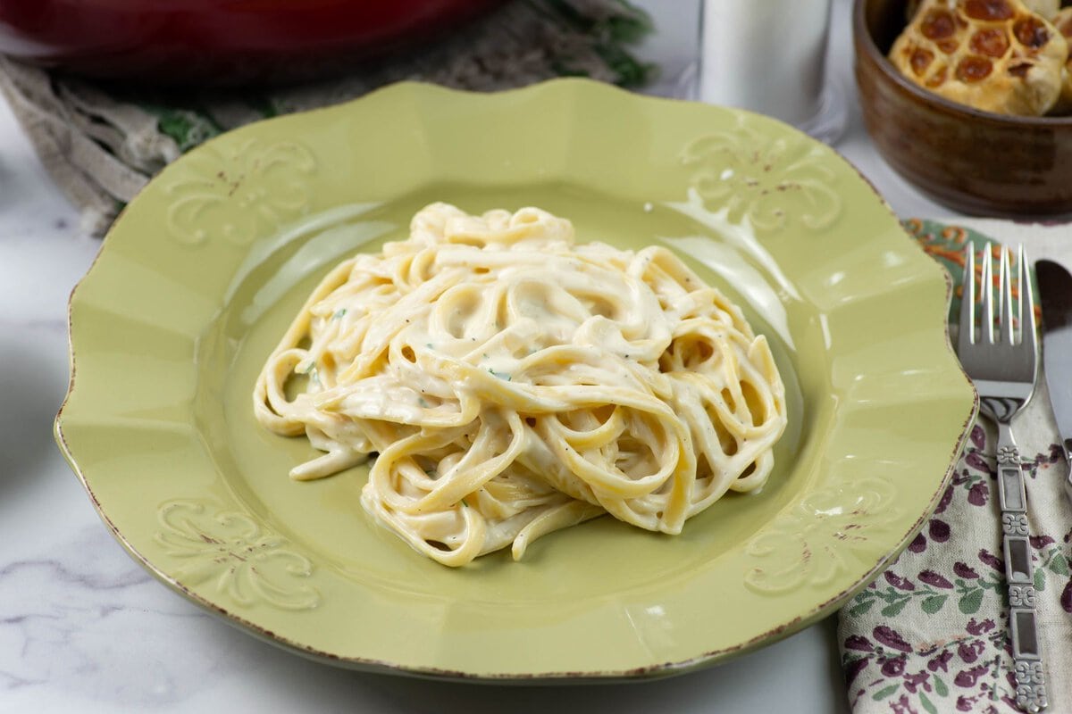 White garlic pasta sauce served over fettuccine pasta on a green dinner plate.