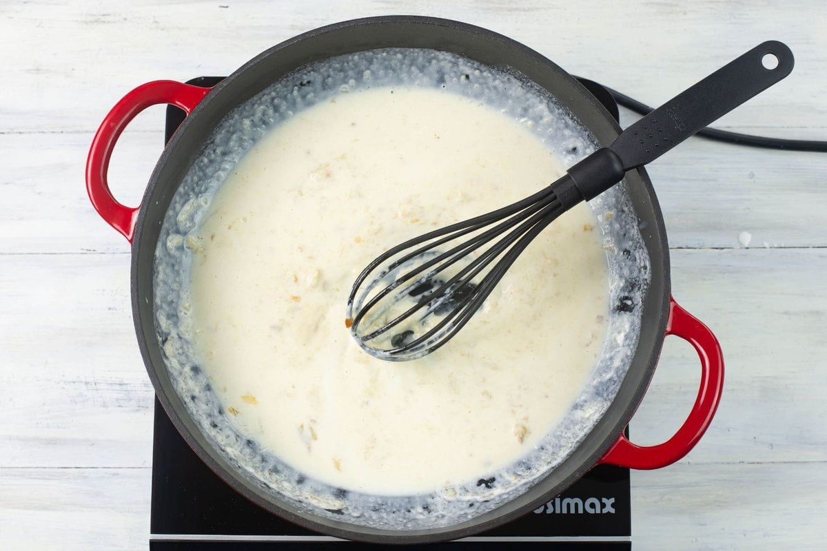 Mixing cream with a roasted garlic roux in a skillet.