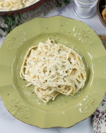 A creamy roasted garlic alfredo served over pasta on a green dinner plate.