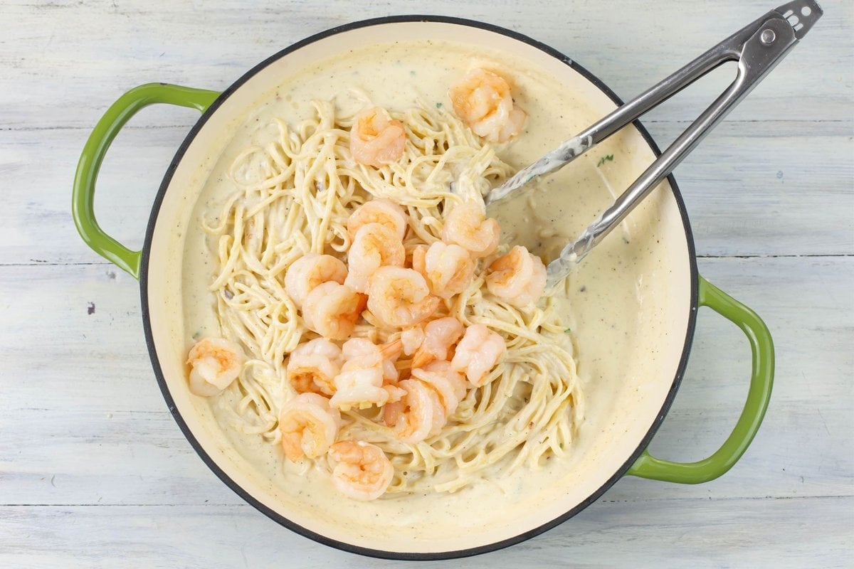 Combining the cooked shrimp with alfredo sauce and pasta.