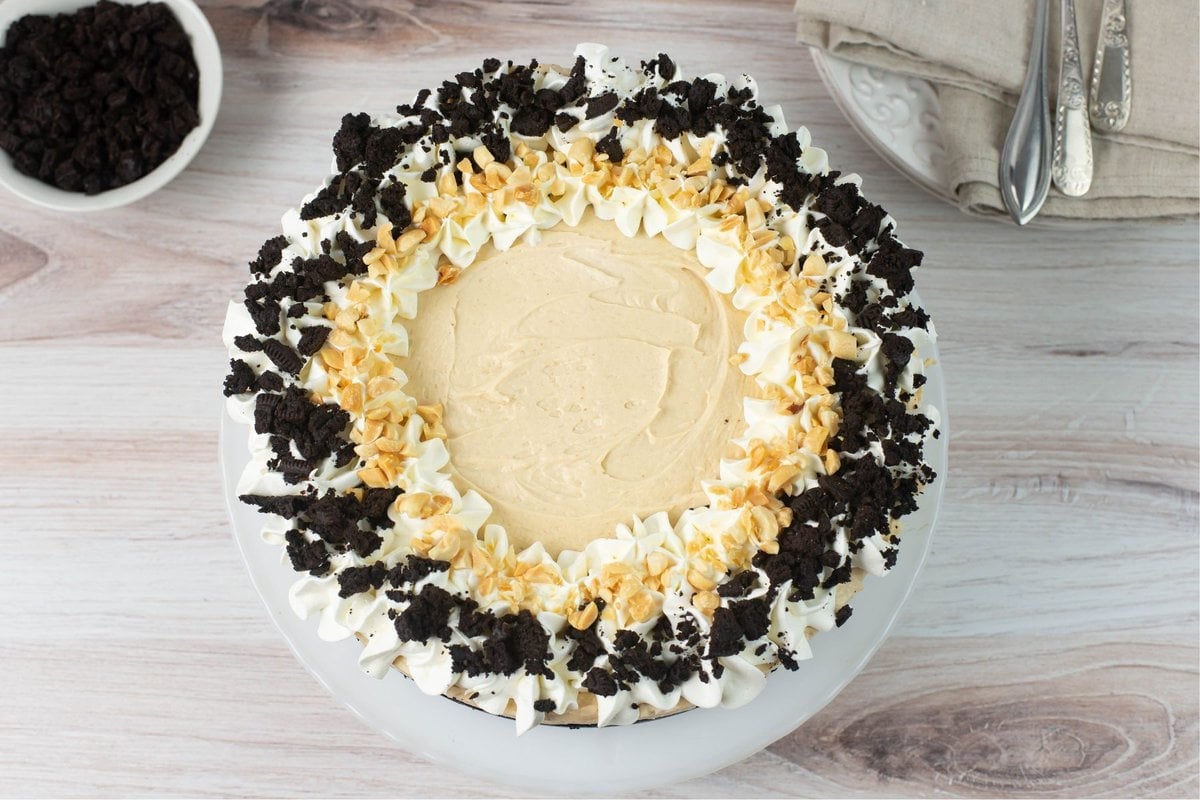 Over head image of the uncut Peanut Butter Cheesecake decorated with whipped cream, crushed cookies and crushed peanuts.