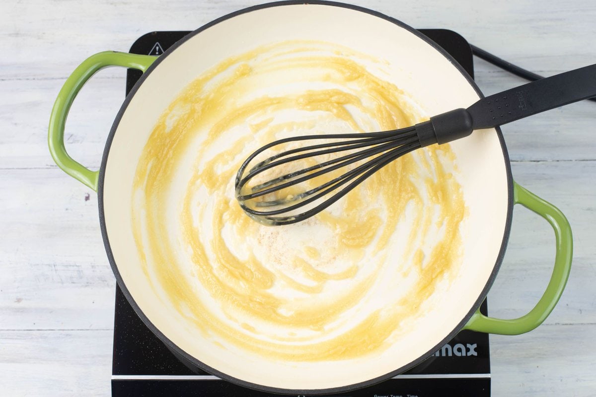 Whisking flour and melted butter together in a cast iron skillet to make a roux.