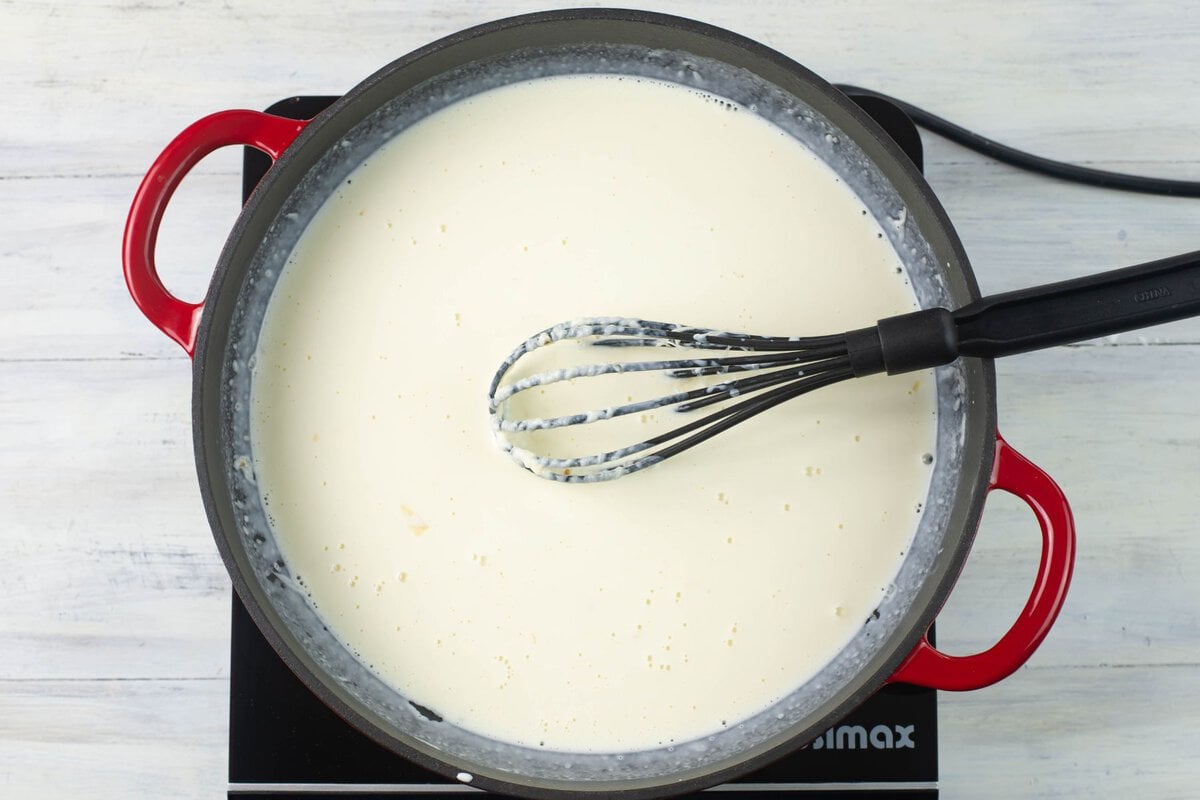 Whisking garlic alfredo sauce until the cheese has melted and blended into the sauce.