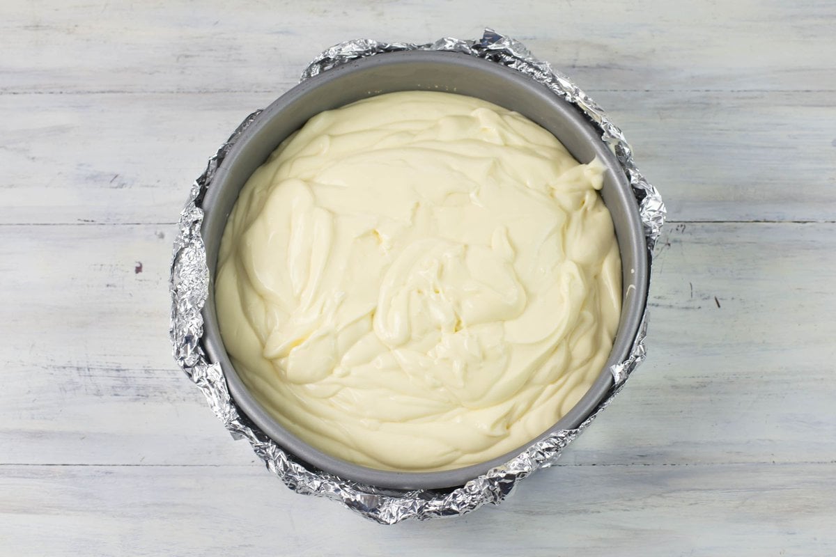 White chocolate cheesecake filling poured into a springform pan wrapped in aluminum foil to bake in a Bain Marie method.
