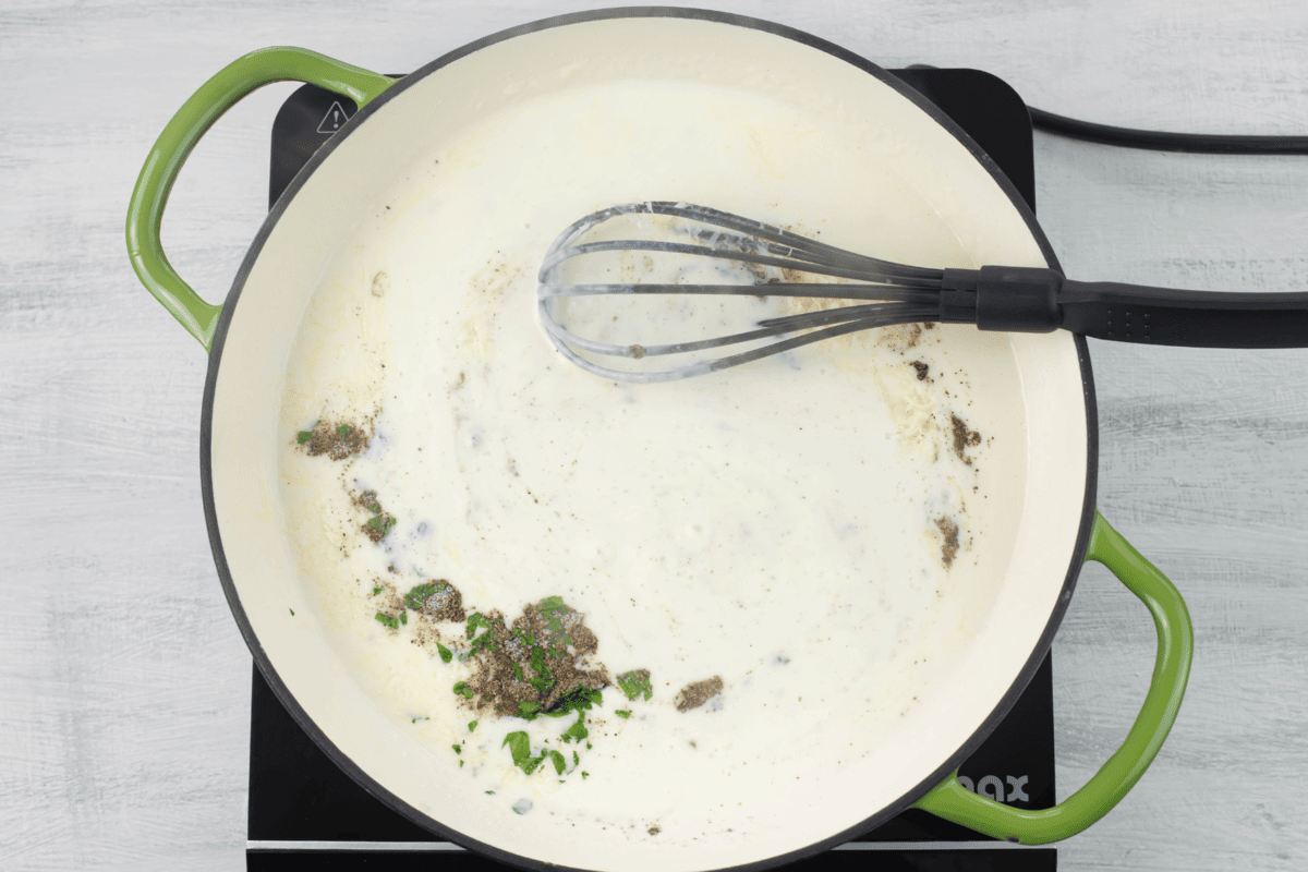 Adding the seasonings to the skillet of alfredo.