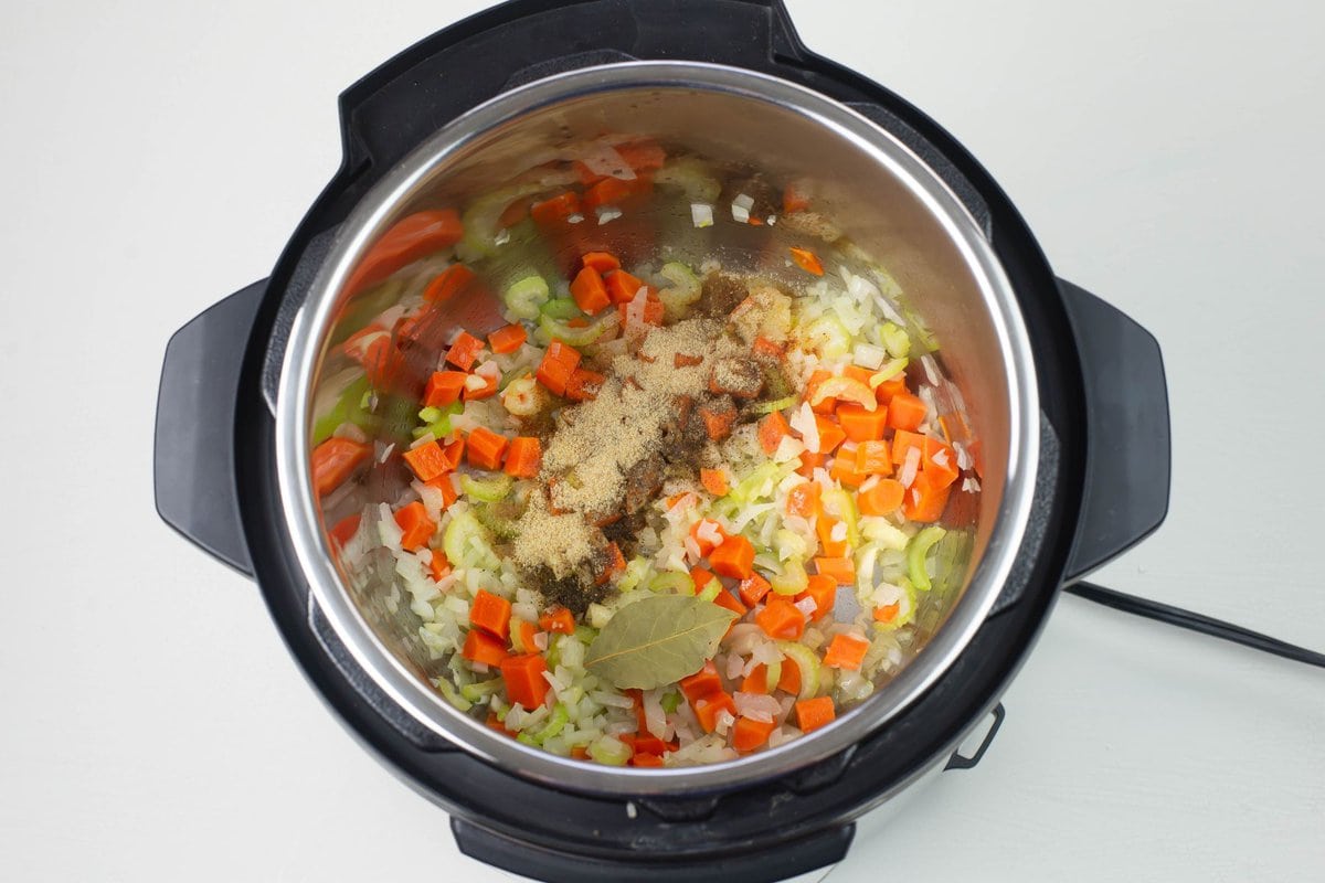 Overhead image of the inner pot adding the herbs and spices to the vegetables.
