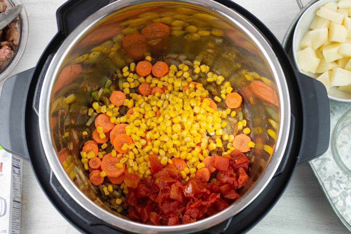 Adding the carrots, corn and tomatoes to the pot.