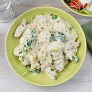 A bowl filled with creamy chicken tortellini alfredo on a table.