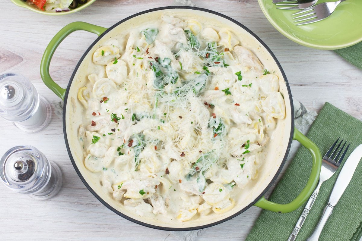 Overhead image of an enamel skillet filled with chicken tortellini alfredo on the dinner table.
