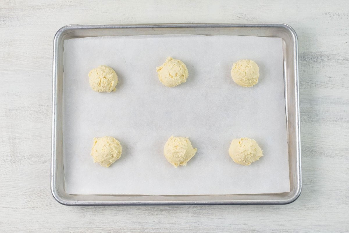 Six 1 ½ inch cookie dough balls on a baking sheet.