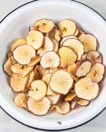 Dehydrated Apple Slices in a large bowl with step by step directions how to make.