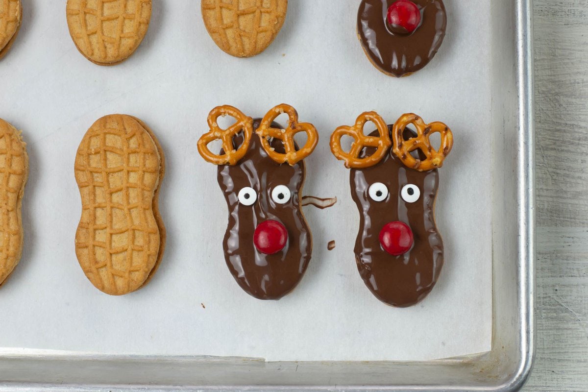 Chocolate dipped and decorated reindeer cookies on a lined cookie sheet.