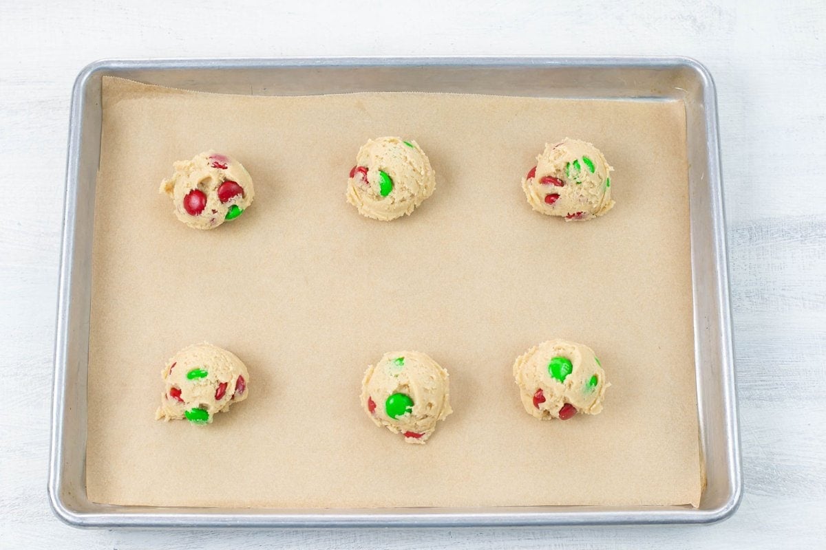 M&M cookie dough balls on a lined cookie sheet.