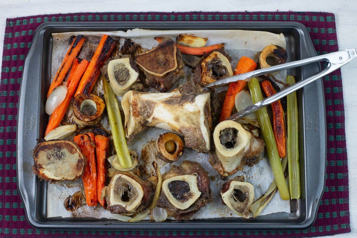 Roasted beef broth bones, carrots, celery, onion and garlic on a large sheet pan.