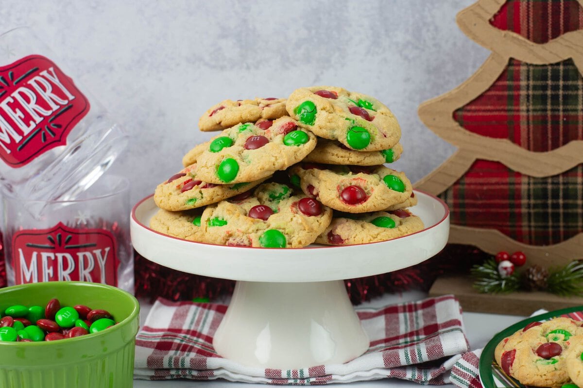 Serving a stack of M&M Christmas cookies on a white cake stand.