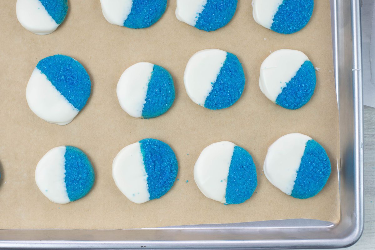 Closeup white chocolate dipped blue Christmas cookies on a baking sheet.