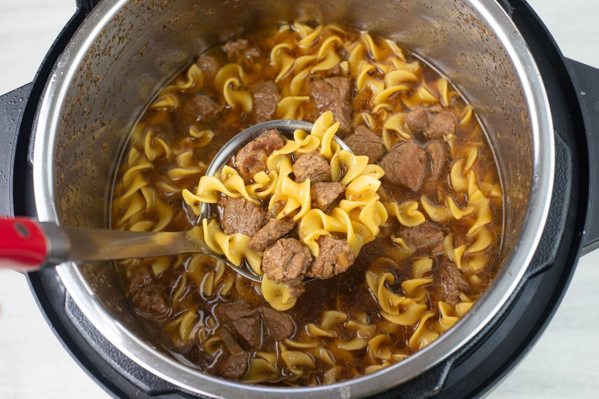 A ladle full of cooked egg noodles with beef and gravy.