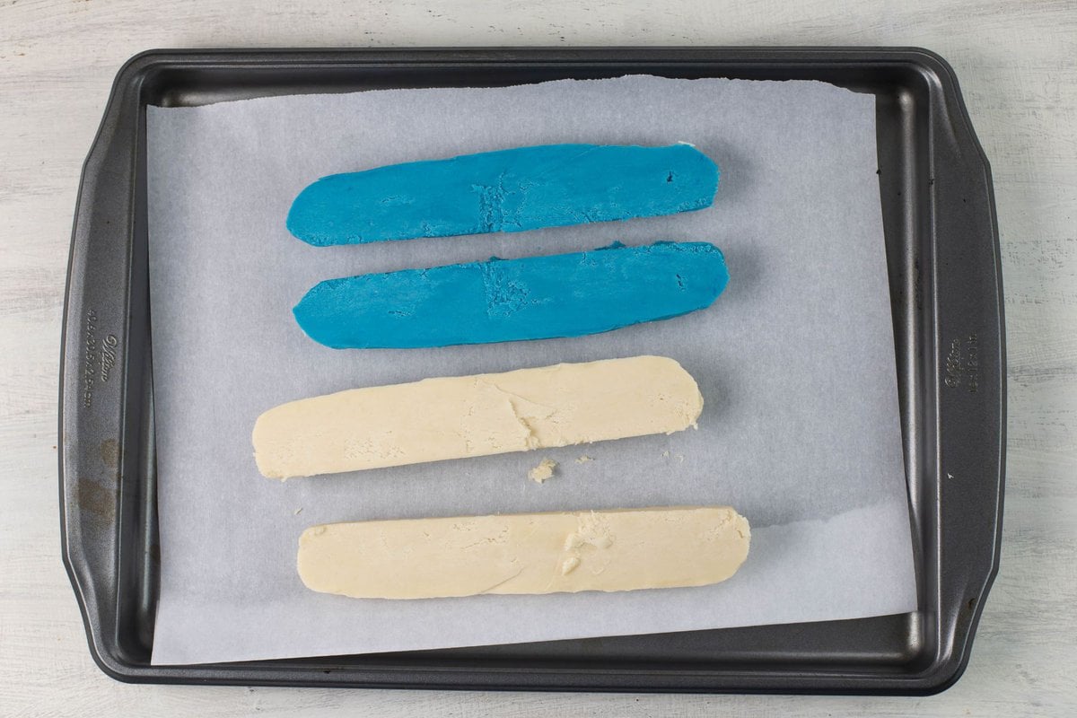 The blue and white cookie dough logs cut in half on a cookie sheet.
