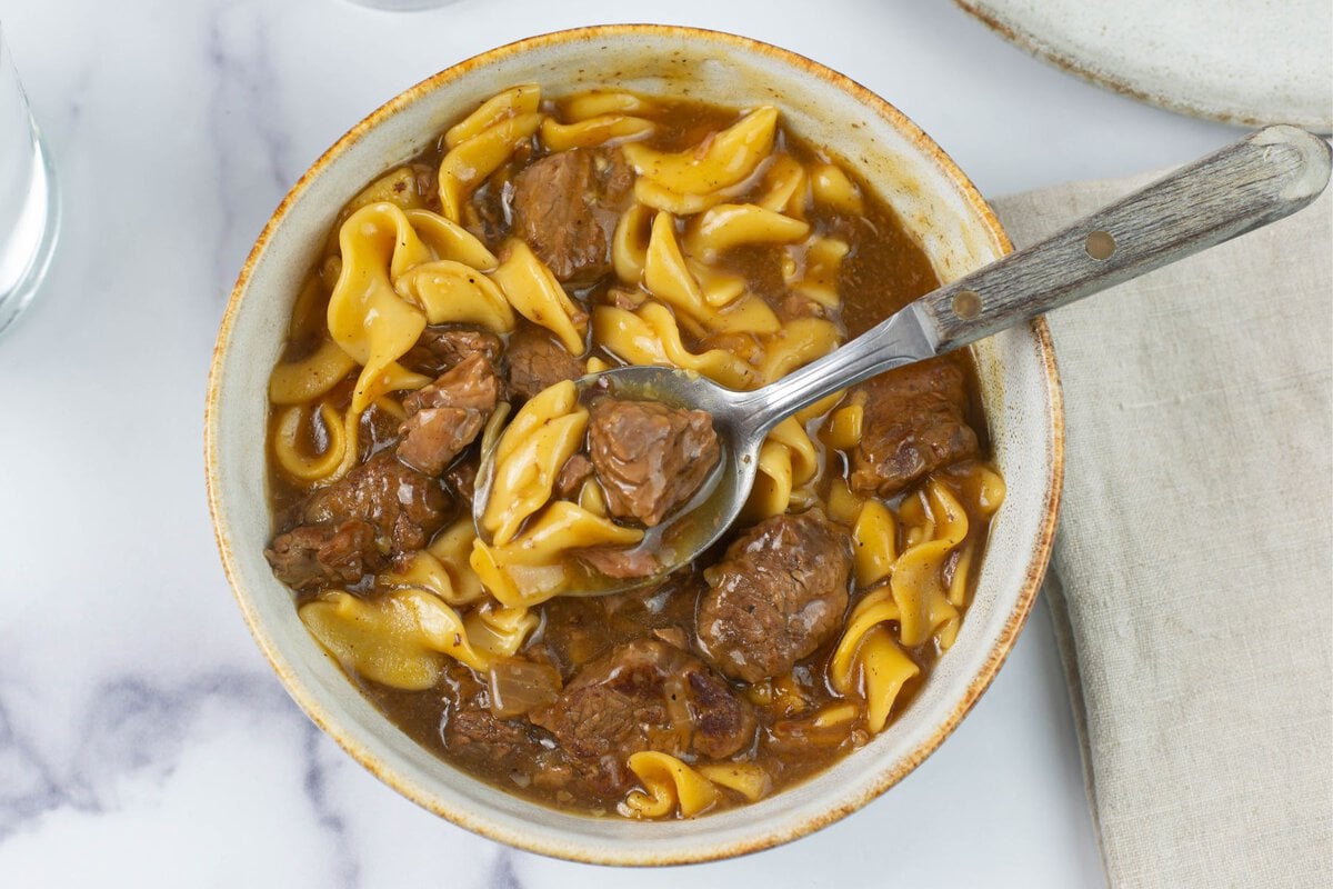 Tender chunks of beef, and wide egg noodles in a rich beef gravy served in a bowl.